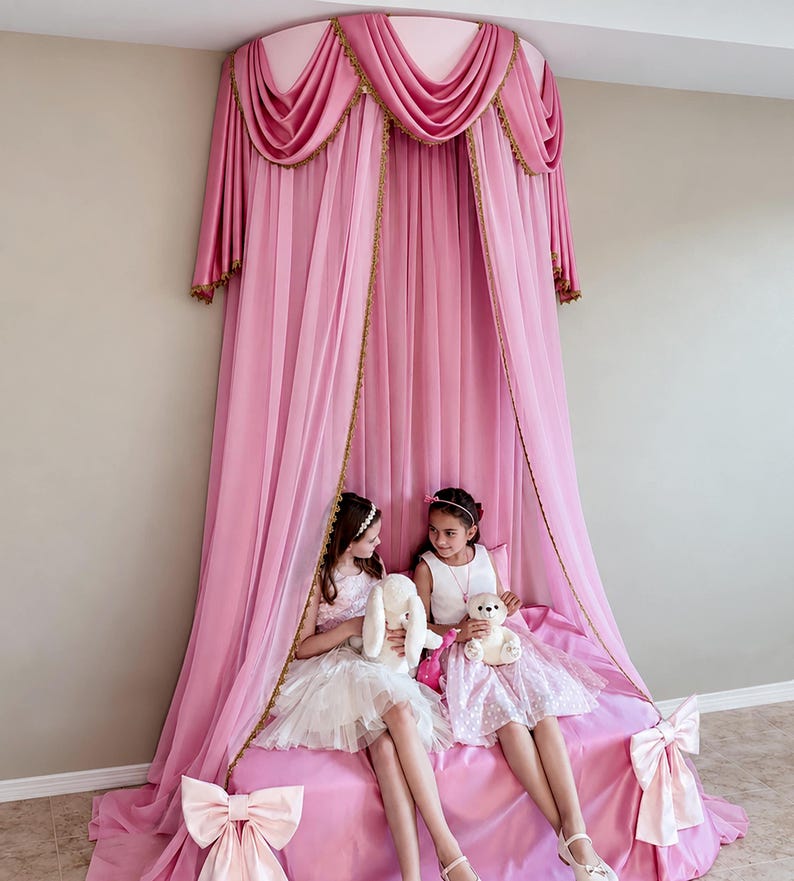May include: A pink bed canopy featuring a circular top mount with draped fabric panels, gold trim accents, and two large decorative bows attached to the lower corners of the bed skirt. The sheer pink curtains hang from the ceiling to the floor.