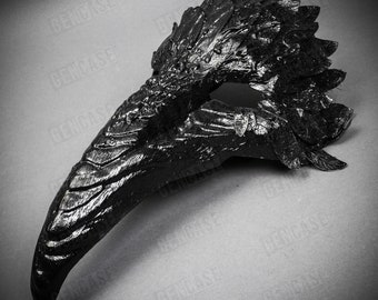 Op de afbeelding: Een zwart masker voor een maskerade met een lange, gebogen snavel en een getextureerd, gevederd ontwerp. Het masker is gemaakt van plastic en is ontworpen om de ogen en neus te bedekken.