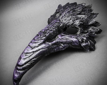May include: A black and purple masquerade mask with a long, curved beak and feathery details. The mask is made of a textured material that resembles feathers.