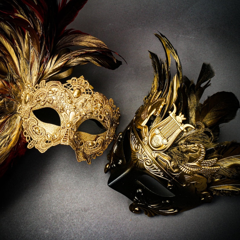 Puede incluir: Dos m&aacute;scaras doradas ornamentadas para carnaval con dise&ntilde;os intrincados y adornos de plumas. Una m&aacute;scara es principalmente dorada con plumas rojas y marrones, la otra es negra y dorada con un dise&ntilde;o cl&aacute;sico.