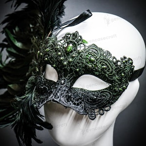 Peut inclure: Un masque de mascarade en dentelle noire et verte avec des plumes. Le masque pr&eacute;sente des motifs floraux complexes, des pierres pr&eacute;cieuses vertes et des plumes noires sur le c&ocirc;t&eacute; gauche. Un ruban noir maintient le masque.