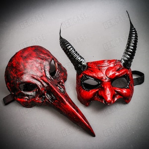 May include: Two red masquerade masks with black accents. One mask has a long, pointed nose and the other has horns.