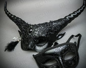 May include: A pair of black masquerade masks. One mask has a horned design with black lace and a black feather. The other mask has a traditional Venetian design with black glitter.