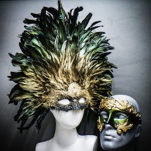 Pode incluir: Duas máscaras de baile de máscaras ornamentadas. Uma máscara é dourada e preta com um grande cocar de penas. A outra máscara é dourada e verde com filigrana decorativa. Ambas as máscaras são exibidas em cabeças de manequim.