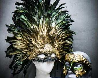 Puede incluir: Dos máscaras de mascarada ornamentadas. Una máscara es dorada y negra con un gran tocado de plumas. La otra máscara es dorada y verde con filigranas decorativas. Ambas máscaras se exhiben en cabezas de maniquí.