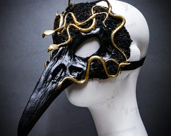 May include: A black plague doctor mask with a long beak and eye openings. The mask is adorned with gold-colored snakes. The mask is made of textured material and has a black strap.
