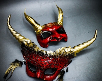 May include: Two devil-themed masquerade masks. The top mask is red with gold horns. The bottom mask is red with gold accents, feathers, and gold horns. Both masks have eye holes and are designed for a costume or theatrical use.