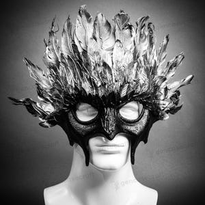 Könnte beinhalten: Eine schwarze Maskenballmaske mit einem Federdesign. Die Maske hat eine spitze Nase und Augenlöcher. Die Federn sind silber und schwarz.