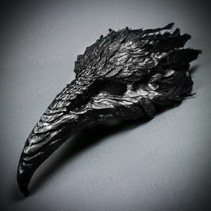 K&ouml;nnte beinhalten: Schwarze Rabenmaske mit langem Schnabel und Federn. Die Maske ist aus einem strukturierten Material gefertigt und wirkt realistisch.
