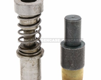 May include: Two metal components, likely for a machine or tool. One has a spring and a cylindrical top with a hole. The other is a solid cylinder with a brass-colored base.