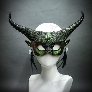 以下が含まれることがあります： 緑と黒の角のあるマスク。装飾的なレースのデザイン、宝石のアクセント、クリスタルと羽の装飾が揺れています。 マスクには湾曲した角があり、白いマネキンの頭に表示されています。 マスクはおそらくコスチュームまたは仮面舞踏会用です。