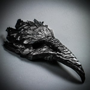 K&ouml;nnte beinhalten: Eine schwarze Rabenmaske mit einem detaillierten Federdesign. Die Maske hat einen langen, spitzen Schnabel und eine strukturierte Oberfl&auml;che.
