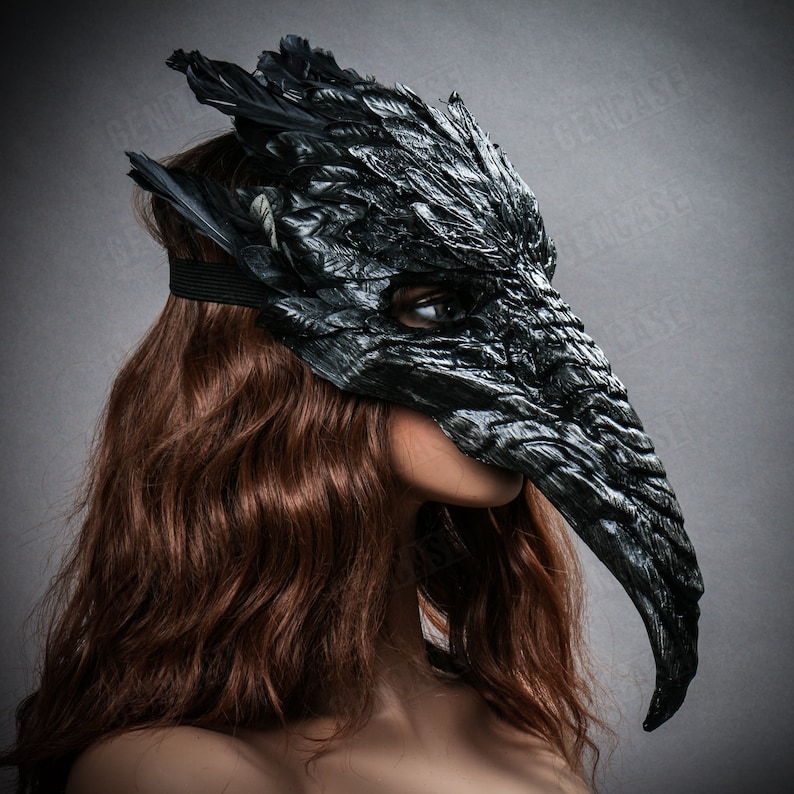 K&ouml;nnte beinhalten: Eine schwarze Maskenballmaske mit einem langen, gebogenen Schnabel und Federnverzierungen. Die Maske ist aus einem strukturierten Material gefertigt, das Leder oder Federn &auml;hnelt.