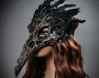 Op de afbeelding: Een gedetailleerd ravenmasker met een lange, getextureerde snavel en ingewikkelde veerdetaillering. Het masker is voornamelijk zwart en brons, met een verweerde afwerking. Het bedekt het gezicht en wordt vastgezet met een zwarte elastische band, ideaal voor kostuums of cosplay.