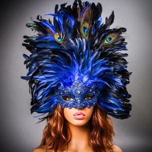 May include: A blue and black masquerade mask with feathers. The mask has a blue and silver lace design and rhinestones. The feathers are arranged in a tall, dramatic headdress.