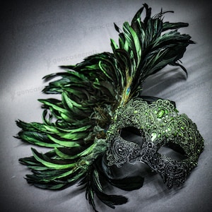 Peut inclure: Un masque de mascarade d&eacute;coratif avec un design demi-visage. Le masque pr&eacute;sente des d&eacute;tails en dentelle noire et verte, orn&eacute;s de pierres pr&eacute;cieuses vertes. De longues plumes vertes et une plume de paon unique accentuent le masque.