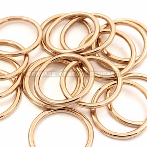 May include: A pile of gold-colored metal rings. The rings are all the same size and shape, and they are arranged in a random pattern.