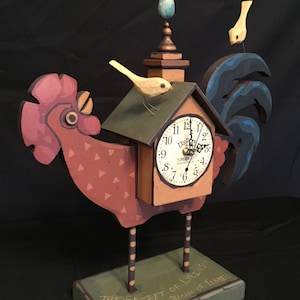 May include: A wooden rooster clock with a small house on its back. The house has a clock face with the words "USPS" and "ZIMMERMANS" on it. The rooster is standing on a base with the words "THE SECRET OF LIFE IS ENJOYING THE PASSAGE OF TIME" on it.