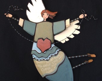 May include: Wooden angel figurine with white wings, brown hair, and a red heart. The angel wears a blue and green dress and holds strings. The text on the dress reads: "Small things done with great love will change the world."