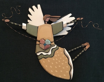 May include: A whimsical wooden angel with wings, holding two strings in its hands. The angel is painted in shades of brown, green, and white, with a heart-shaped design on its chest. The text "HEART-CENTERED" is written on the angel's skirt.