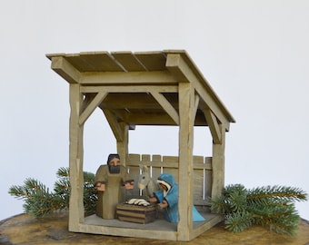 May include: A wooden nativity scene with a gray wooden stable, a brown wooden manger, a gray wooden figure of Joseph, a blue wooden figure of Mary, and a white wooden figure of a donkey.