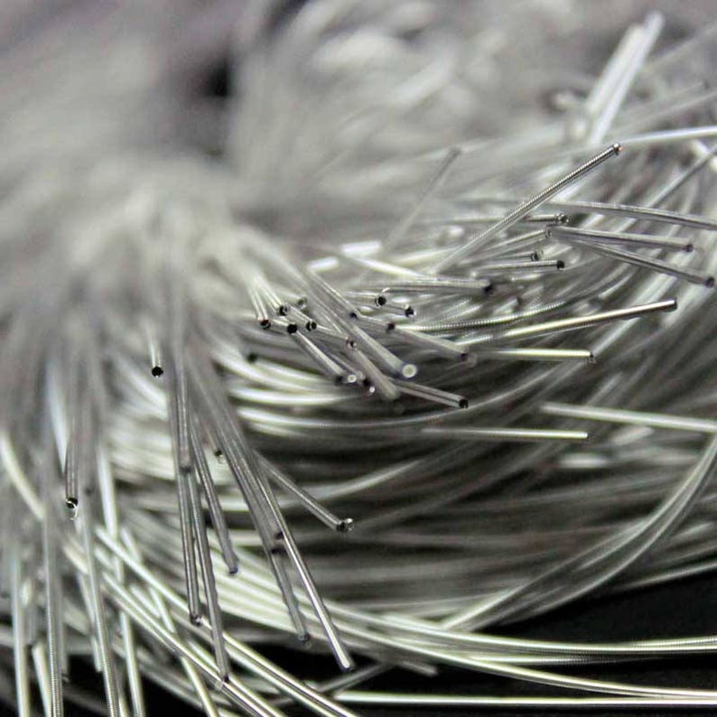 May include: Close-up of a bundle of thin, silver-colored metal tubes. The tubes are clustered together, with some extending outwards. The ends of the tubes appear to be hollow. The background is blurred, creating a soft focus.