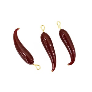 May include: Three red glass chili pepper charms with gold-colored metal loops. The charms are shaped like chili peppers and have a glossy finish.