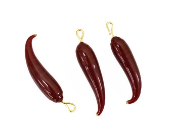 May include: Three red glass chili pepper charms with gold-colored metal loops. The charms are shaped like chili peppers and have a glossy finish.