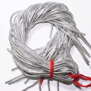 May include: A coil of silver-coloured wire, bound with red string. The wire is flexible and has a metallic sheen, possibly for crafts or jewellery. The background is plain white. The wire is likely measured in centimetres.