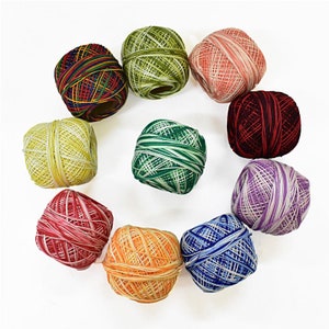 May include: A collection of ten colorful balls of embroidery floss arranged in a circle. The floss colors include red, green, yellow, orange, blue, and purple. Each ball is tightly wound, showcasing the various hues and patterns of the thread.