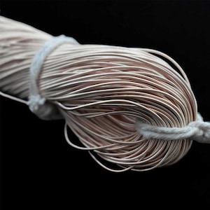 May include: Close-up of a bundle of thin, light brown wire, tightly wound and secured with a white cord. The wire has a metallic sheen, and the background is solid black.