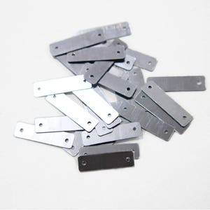 May include: A pile of silver metal rectangular tags with two holes in each tag.