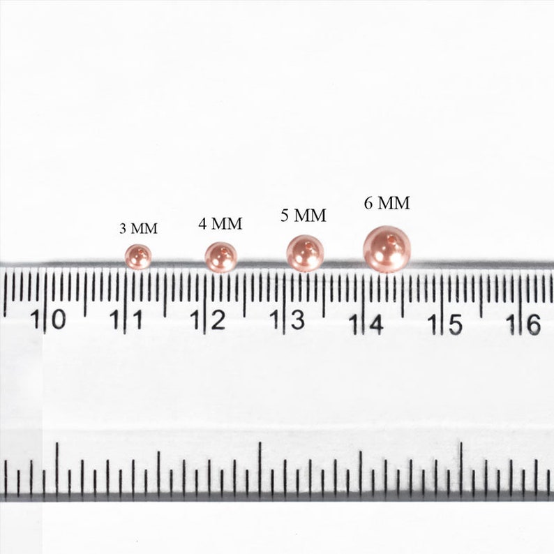 May include: A ruler with four rose gold colored metal beads of different sizes. The beads measure 3 mm, 4 mm, 5 mm, and 6 mm in diameter.
