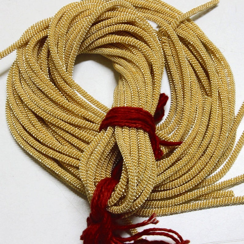 May include: A bundle of gold-colored cord with a red string tied around it. The cord is made of small beads and is perfect for crafting projects.