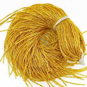 Op de afbeelding: Een bundel glanzend gouden metallic koord, strak opgerold en vastgezet met een wit touwtje. Het koord heeft een getextureerd, geribbeld uiterlijk en reflecteert licht. Ideaal voor knutselen, sieraden maken of decoratieve doeleinden.