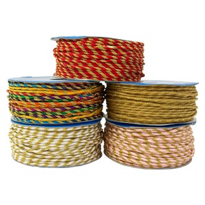 May include: A stack of six spools of decorative twisted cord in various colors. The colors include red and gold, multi-colored, gold, white and gold, and pink and gold. The cord is wound on blue spools.