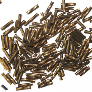 Op de afbeelding: Een grote hoeveelheid goudkleurige metalen kralen. De kralen zijn lang en dun, met een gedraaide of geribbelde textuur.