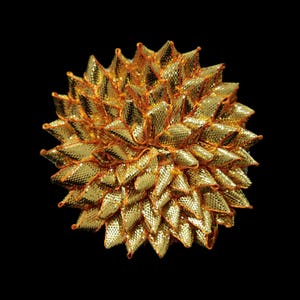 May include: A gold and orange decorative flower made of fabric. The flower has a 3D, spiky appearance.