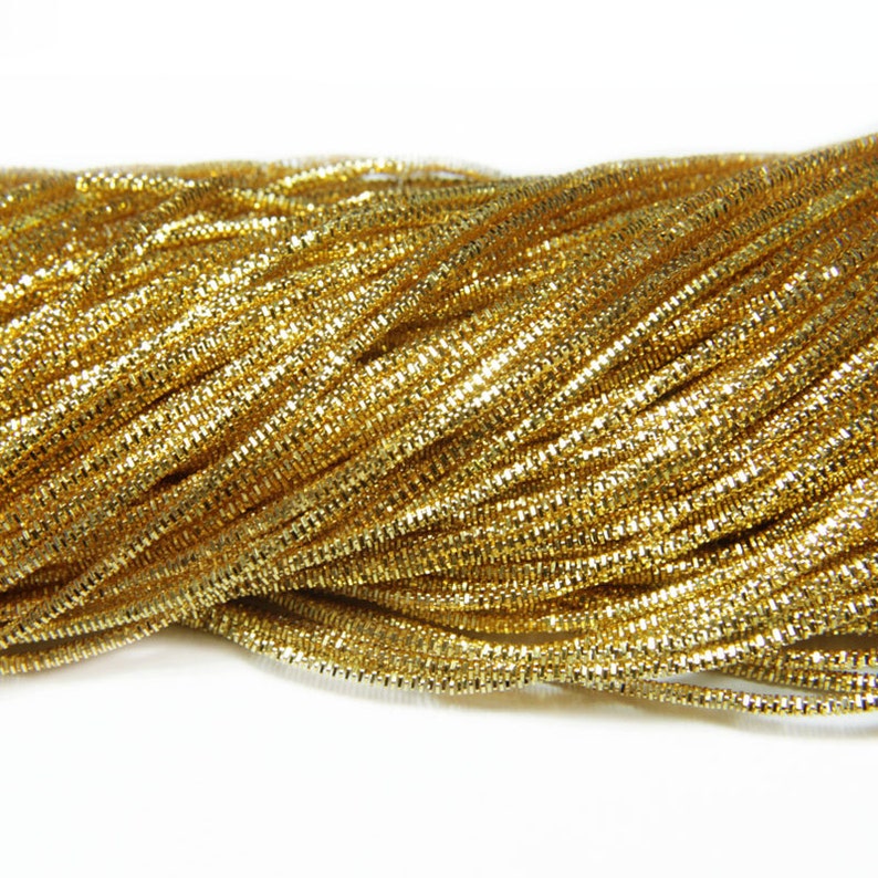 May include: A close-up of a pile of gold metallic cord. The cord is shiny and has a slight sparkle.
