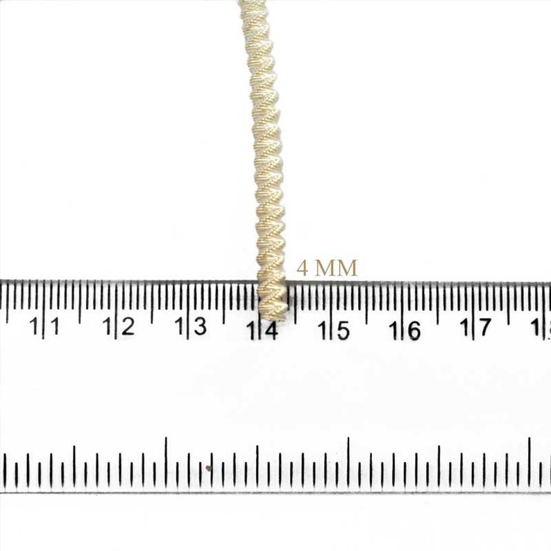 May include: A close-up of a cream-colored braided trim with a ruler showing it is 4 mm wide.