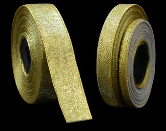 May include: Two spools of gold ribbon against a black background. The ribbon has a shimmering, textured appearance. The spools are partially unrolled, revealing the ribbon's width and the inner core. Ideal for crafts and gift wrapping.