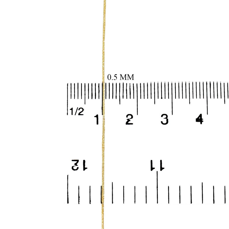 May include: A close-up of a gold cord or thread measured against a ruler. The ruler is marked in 1/2 inch increments and 0.5 mm increments. The cord is approximately 0.5 mm thick.