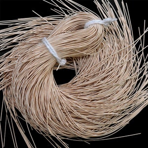 May include: A bundle of thin, beige-colored wire, tightly wound and secured with a white string. The wire is arranged in a circular pattern, with loose strands extending outwards against a black background. This item is suitable for jewelry making and crafts.
