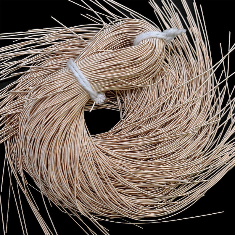 May include: A bundle of thin, beige-colored wire, tightly wound and secured with a white string. The wire is arranged in a circular pattern, with loose strands extending outwards against a black background. This item is suitable for jewelry making and crafts.
