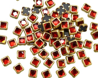 Könnte beinhalten: Ein Haufen roter quadratischer Strasssteine mit goldenen Fassungen. Die Strasssteine sind auf einem weißen Hintergrund verstreut.