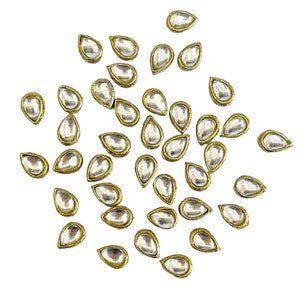 Puede incluir: Una colección de adornos de vidrio transparente en forma de lágrima con un borde de metal dorado. Estos elementos decorativos están dispersos sobre un fondo blanco, mostrando sus superficies reflectantes.