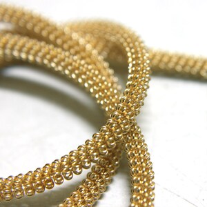 May include: A close-up of a gold chain necklace made of small, linked rings. The chain is twisted and looped, creating a decorative and intricate design.