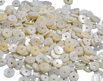 May include: A pile of white, round, mother of pearl shell beads with a hole in the center. The beads are smooth and have a slight iridescent sheen.
