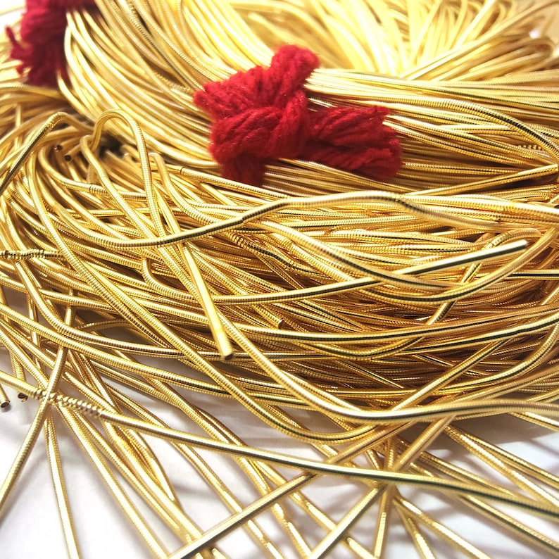 May include: A close-up of a pile of gold-colored, flexible, metal cord. The cord is coiled and twisted, creating a textured and intricate pattern.