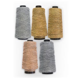 May include: Five spools of metallic thread in silver, gold, and rose gold. The thread is wound around a black plastic spool.